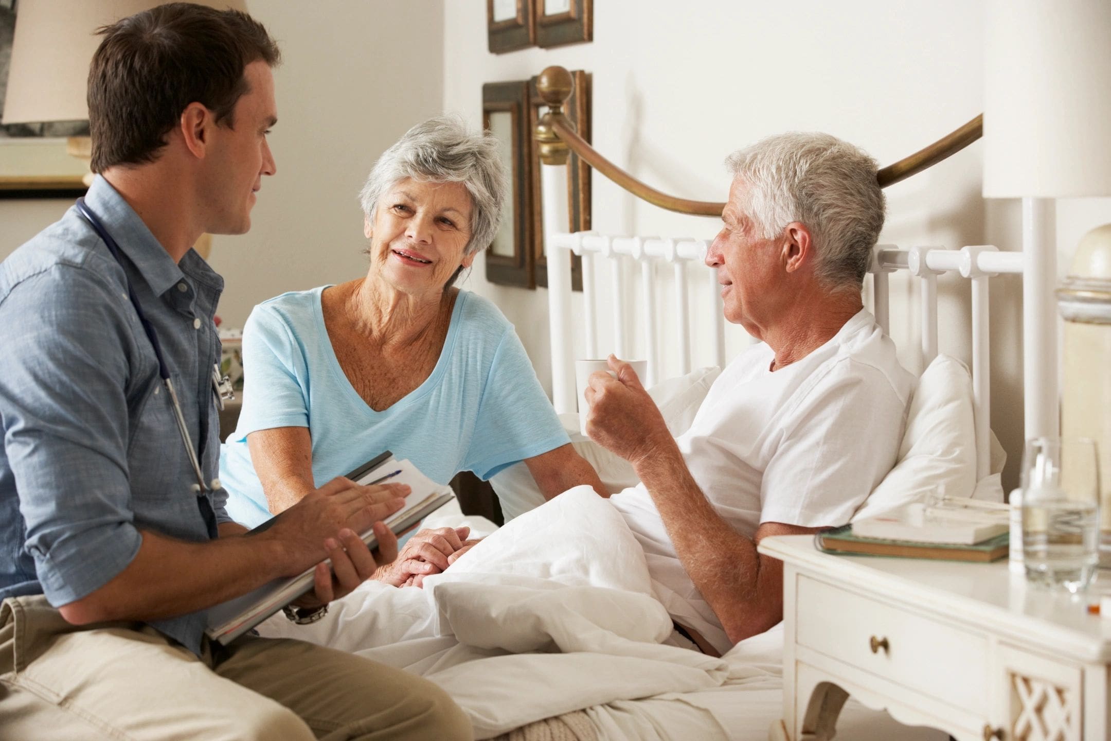 A man and two women sitting on the bed talking to an older gentleman.